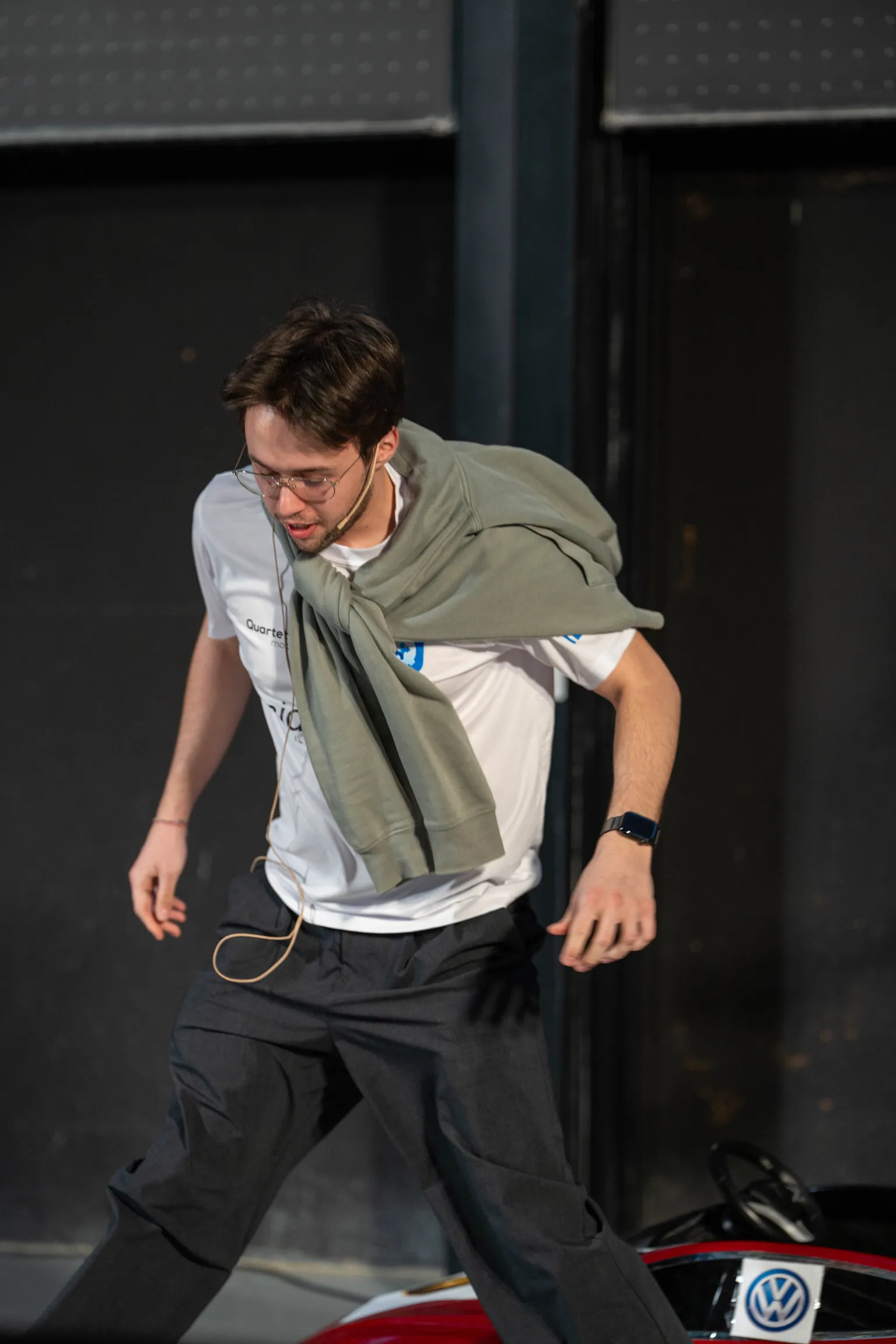 Justin walking on stage during the CAT theatre scene, earpiece in place, Tesla prop visible behind