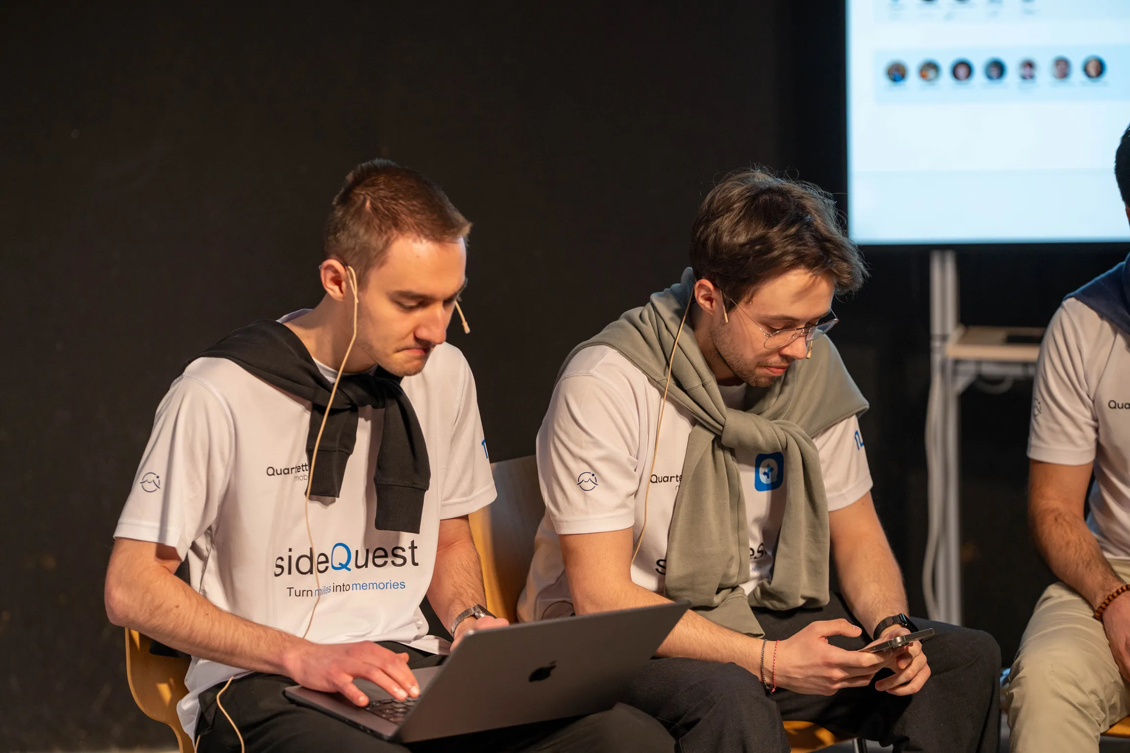 Two sideQuest teammates seated on stage with laptops during the CAT theatre scene