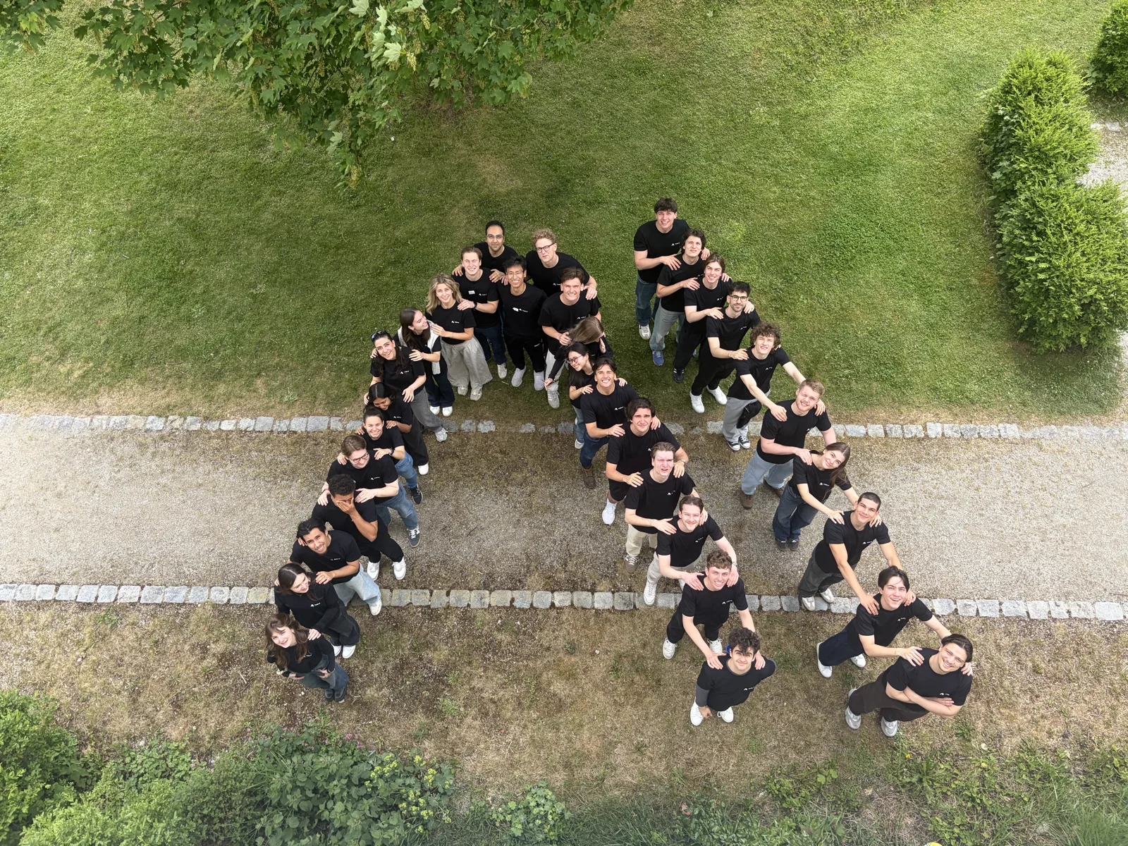 Luftaufnahme von rund fünfunddreißig TUM.ai-Mitgliedern, die auf einem Weg eine Formation bilden, von oben gesehen.